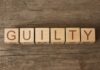 Wooden blocks spell out "GUILTY" on wood background.