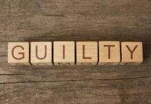 Wooden blocks spell out "GUILTY" on wood background.