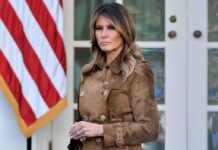 Woman in brown coat near American flag.