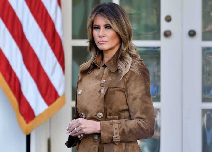 Woman in brown coat near American flag.