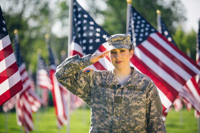 1081070213 featured image Saluting soldier in uniform with American flags background.