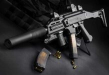 Black assault rifle with silencer and magazine on dark background.