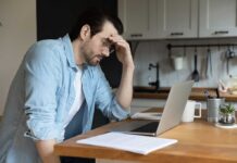 Man stressing over work on laptop at kitchen table