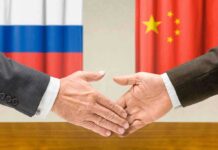 Handshake in front of Russian and Chinese flags