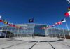 Flags outside NATO headquarters building under clear blue sky