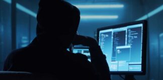 Person in hoodie working at computer in dark room