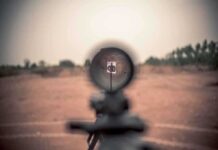Rifle scope aimed at a distant target outdoors