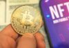 Person holding Bitcoin coin NFT text on screen