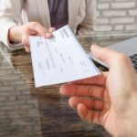 Hands exchanging a check near a laptop