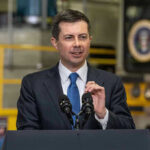 Buttigieg UNDER FIRE: Tax Dollars Funneled to DEI Man in suit speaking at a podium indoors