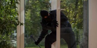 A burglar in dark clothing entering a house through a glass door