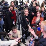 Israel’s Blockade: Gaza Reporters in GRAVE Danger A crowded press conference with journalists and cameras surrounding a speaker