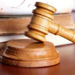 A wooden gavel resting on a circular base with law books in the background