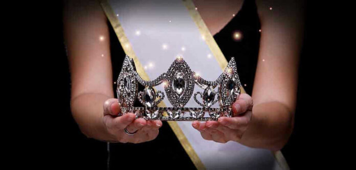 Sash-wearing person holding an ornate jeweled crown.