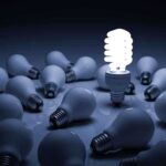 A bright energy-efficient light bulb surrounded by traditional bulbs