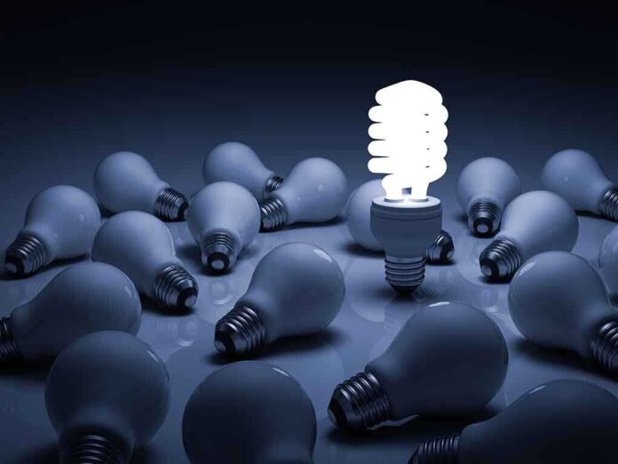 A bright energy-efficient light bulb surrounded by traditional bulbs