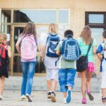 Group of children walking towards a school entrance with backpacks