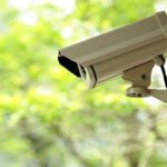 A security camera mounted outdoors with a blurred green background