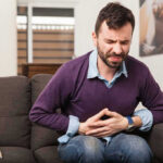 Man sitting on couch, holding stomach in pain.