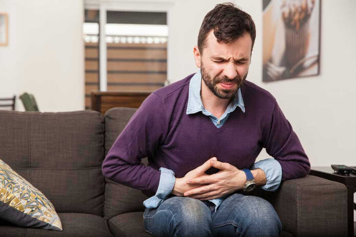 Man sitting on couch, holding stomach in pain.