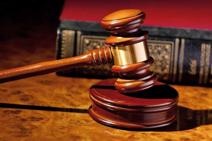 A wooden gavel resting on a polished surface with a law book in the background