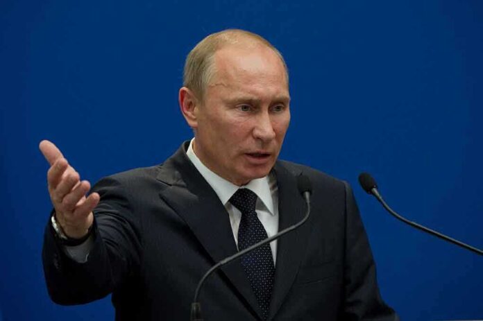 A man in a suit gesturing while speaking at a podium with microphones against a blue background