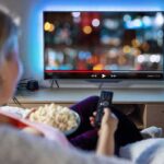 ABC Executives TERRIFIED of Trump Backlash Person sitting on a couch watching a movie on a TV with popcorn in hand