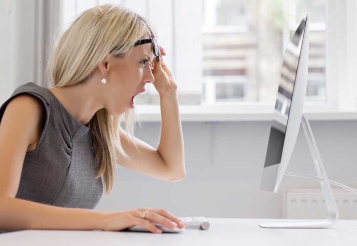 A woman with blonde hair showing a surprised expression while looking at a computer