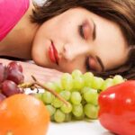 Sleep Saboteurs: The Real Hunger Culprits A woman resting her head on a table surrounded by various fruits