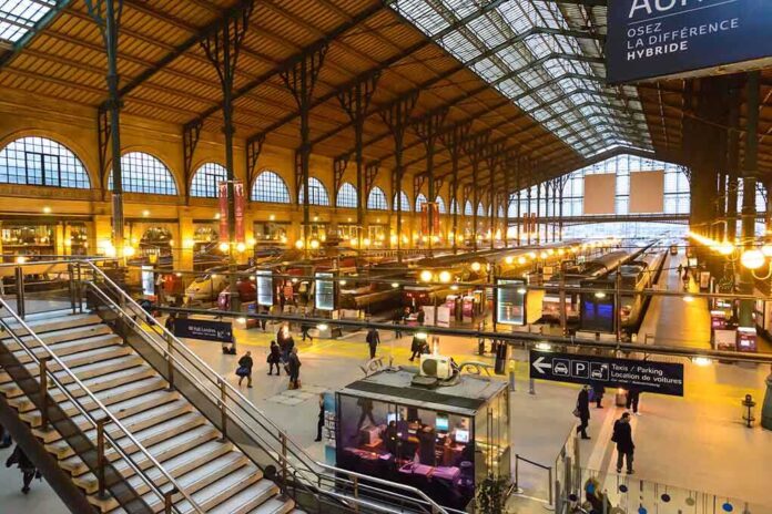 Interior view of a busy train station with large windows and a staircase