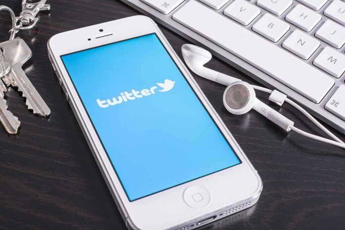 Smartphone displaying the Twitter logo next to keys and earphones on a desk