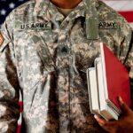 A soldier in a US Army uniform holding books in front of an American flag