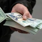 A hand holding a stack of hundred dollar bills with one bill prominently displayed