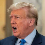 Factory Floor ERUPTION Stuns Trump Tour Man in suit with open mouth, speaking passionately.