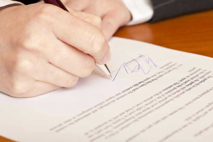 Hand signing a document with a pen.