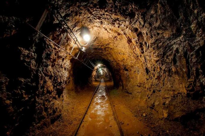 Dimly lit underground tunnel with rail tracks and rocky walls