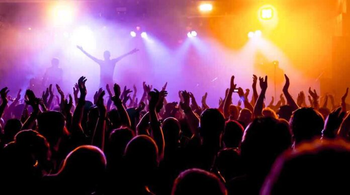 Crowd at a concert with raised hands and colorful stage lights