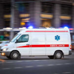 Ambulance driving on urban street with lights flashing.