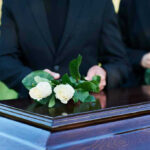 People placing white roses on a casket.