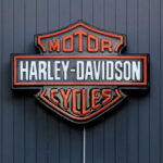 Harley Davidson on Verge of COLLAPSE – Is This The End? Harley-Davidson Motor Cycles logo on dark wall.