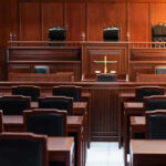 Lawmaker’s Alleged Jury Tactics Unveiled! Empty courtroom with wooden benches and judges bench.