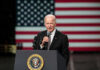Man speaking at podium with US flag background.