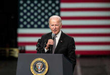 Biden’s Ghostwriter Tapes LEAKED! Man speaking at podium with US flag background.