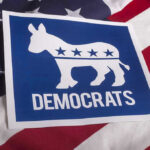 Congress Hopeful Targets American for Concentration Camps! Democrats logo on American flag background