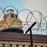 Female Prison Guard ARRESTED – Shocking Rape Claims! Barbed wire in front of a prison tower.