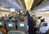 Mid-Flight Mayhem – Passengers TACKLE Maniac! Interior view of an airplane with passengers seated and using in-flight entertainment screens