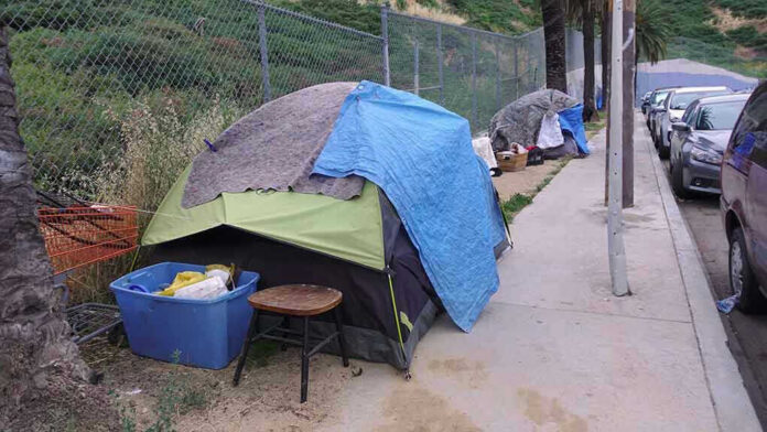1392494762 Tents and belongings set up along sidewalk.