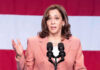 Kamala Makes Pathetic Move in 2028 Desperation Plan Woman speaks at podium with red and white background.