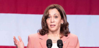 Kamala Makes Pathetic Move in 2028 Desperation Plan Woman speaks at podium with red and white background.