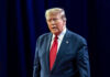 Disgraced Rapper BEGS Trump For Pardon Man in suit with red tie speaking on stage.